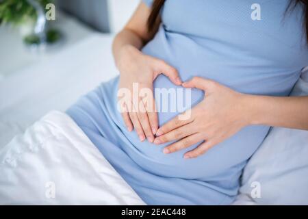 Close up schwangere Frau macht Hand Herz Geste in einem Bett Stockfoto