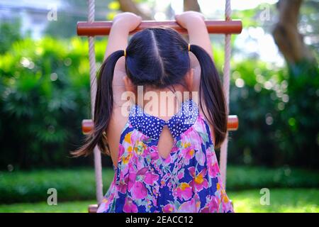 Die Rückansicht eines jungen asiatischen Mädchens spielt auf einem Spielplatz und versucht, eine Leiter zu klettern, die Spaß hat und sich glücklich fühlt, mit grünem Gras und Bäumen in t Stockfoto