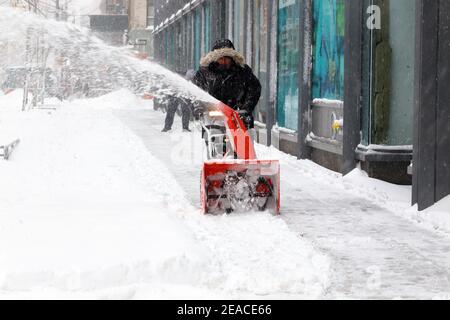 Eine Person nutzt einen Schneefräsen, um nach einem Winterschneesturm in New York, NY, Schnee von einem Bürgersteig zu entfernen. Stockfoto
