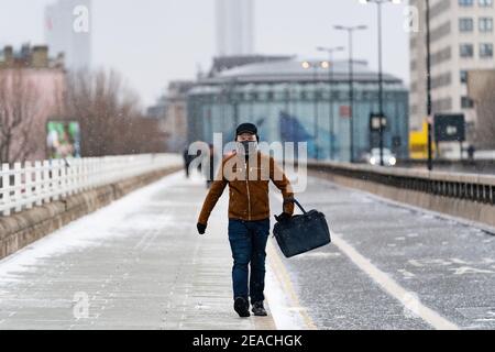 LONDON, ENGLAND - FEBRUAR, 2021: Junger Mann, der die Kamera mit Gesichtsmaske und Gesichtsschild anschaut, läuft auf der Waterloo Bridge in London während eines s Stockfoto