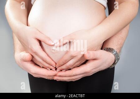 Bauch einer Schwangeren mit Herz aus zwei Paar Händen. Junge weiße Familie wartet auf die Geburt ihres ersten Babys. Schwanger Frau und Mann träumen ein Stockfoto