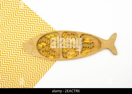 Gelbe Kapseln von Omega 3 liegen auf einem Holzteller In Form des Fisches Stockfoto