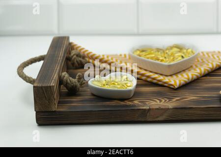 Gelbe Kapseln von Omega 3 liegen auf weißen Keramikplatten In Form der Herzen auf einem Holztablett Stockfoto