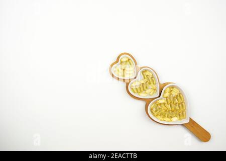 Gelbe Kapseln von Omega 3 liegen auf weißen Keramikplatten In Form der Herzen Stockfoto