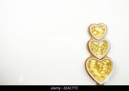 Gelbe Kapseln von Omega 3 liegen auf weißen Keramikplatten In Form der Herzen Stockfoto