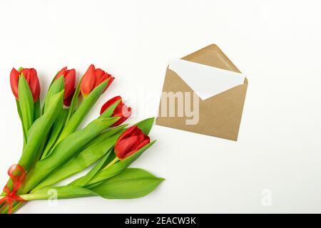 Rote Tulpen und ein leerer Brief in einem braunen Umschlag liegen auf einem weißen Tisch. Modell Stockfoto
