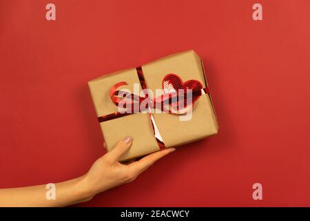 Eine Frauenhand hält eine Geschenkbox mit rotem Herz Und Band darauf Stockfoto