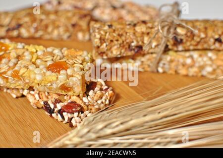 Seitenansicht Nahaufnahme von süßen Scheiben gesunden Getreides Riegel mit getrocknetem Weizen und Früchten auf braunem Holztisch Hintergrund Stockfoto