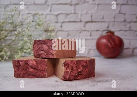 Helle handgemachte Seife und Granat auf einer grauen Arbeitsplatte gegen eine Ziegelwand. Stockfoto
