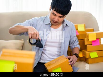 Mann Online-Unternehmer mit Band zum Verpacken Paketkasten im Home Office, bereiten Produkt für die Lieferung an den Kunden, (KMU-Unternehmen) Stockfoto