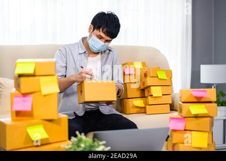 Mann Unternehmer bereiten Paket-Box für die Lieferung an den Kunden zu Hause Büro, er trägt eine Gesichtsmaske für Schutz Coronavirus (covid-19) Pandemie Stockfoto