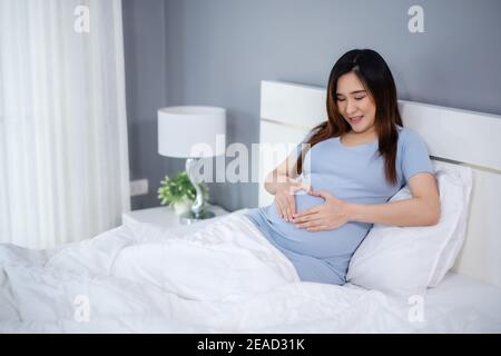 Glückliche schwangere Frau macht Hand Herz Geste in einem Bett Stockfoto
