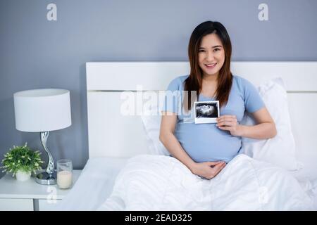 Glückliche schwangere Frau hält Ultraschall Scan Foto auf einem Bett Stockfoto