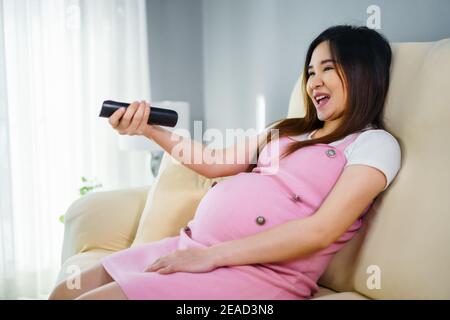 Schwangere Frau beim Fernsehen mit Fernbedienung auf dem Sofa Das Wohnzimmer Stockfoto