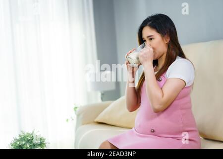 Schwangere Frau trinkt ein Glas Milch auf dem Sofa in Das Wohnzimmer Stockfoto