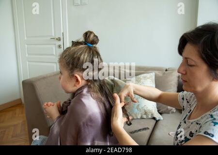 Junge Frau schneidet ihre Tochter die Haare zu Hause während der Pandemie. Bleiben Sie zu Hause. Stockfoto