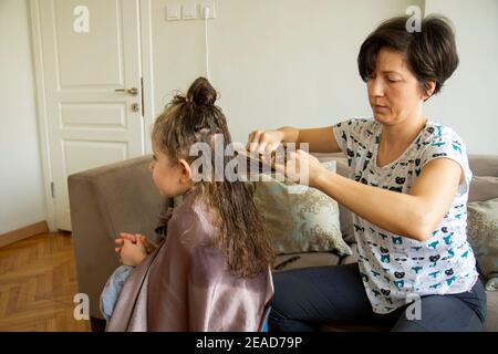 Junge Frau schneidet ihre Tochter die Haare zu Hause während der Pandemie. Bleiben Sie zu Hause. Stockfoto