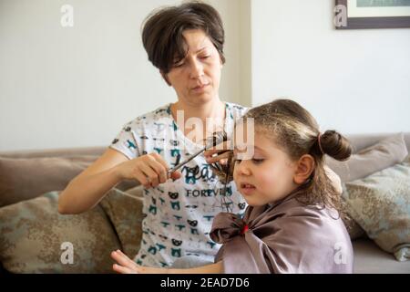 Junge Frau schneidet ihre Tochter die Haare zu Hause während der Pandemie. Bleiben Sie zu Hause. Stockfoto