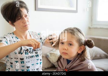 Junge Frau schneidet ihre Tochter die Haare zu Hause während der Pandemie. Bleiben Sie zu Hause. Stockfoto