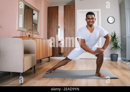 Vorderansicht eines lächelnden, starken afroamerikanischen Mannes, der einen seitlichen Ausfallschritt macht Sport zu Hause Stockfoto