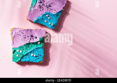 Gefärbtes Einhorn geröstetes Brot mit farbigem Frischkäse auf rosa Hintergrund. Stockfoto