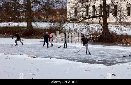 Hørsholm, Dänemark, 8th. Februar 2021. Fünf junge Freunde haben das Eis für Schnee geräumt und genießen ein erfrischendes Eishockey-Spiel auf dem gefrorenen See. Es ist eine seltene und willkommene gesunde Bewegung und Zeitvertreib in diesen Corona Sperrzeiten, wo alle Indoor-Sportanlagen geschlossen sind. Der Palastsee, Slotssøen, hat die erforderliche Eisdicke von mehr als 13 cm erreicht und ist nun erstmals seit 2012 für den Zugang und das Schlittschuhlaufen geöffnet. Stockfoto