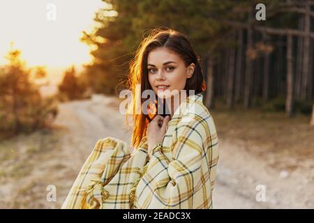 Hübsche Frau im Wald auf der Straße mit einem Decke auf den Schultern bei Sonnenuntergang Stockfoto