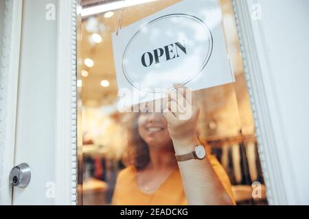 Geschäftseigentümer hält ein Schild, das an der Ladentür geöffnet werden kann. Frau hängt ein offenes Schild an ihre Ladentür. Stockfoto