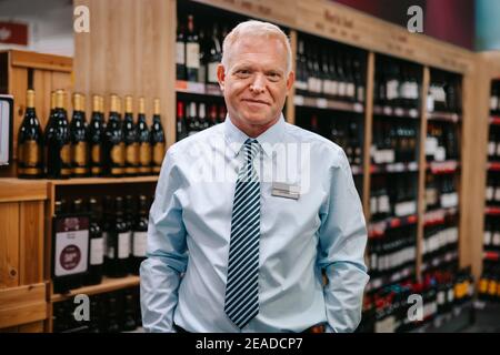 Porträt eines erfahrenen Sommeliers, der im Weinladen steht. Supermarkt Spirituosenabteilung Manager Blick auf die Kamera. Stockfoto