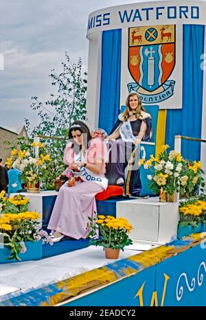 Ein Festwagen mit ‘Miss Watford’ und ihrer Ehrenfrau bei der jährlichen Pfingstparade, Watford, Hertfordshire, England, Großbritannien 1973. Die Frau ist in ihrem zeremoniellen Gewand und trägt die Schärpe ihres Siegers. Hinter ihr ist Watfords Wappen. Das Motto lautet ‘Audentior’, was ‘mit größerer Kühnheit’ bedeutet (aus Vergils Aeniad). Stockfoto