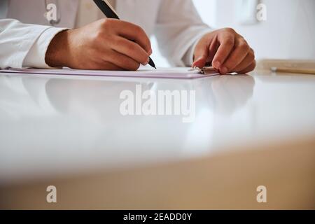 Fokussiertes Bild des Arztes, der Notizen macht, während er am sitzt Schreibtisch Stockfoto