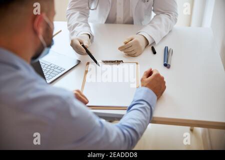 Fokussiertes Bild des Arztes, das sauberes weißes Papier zeigt und hält Bleistift in der Hand Stockfoto