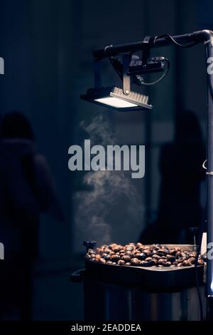 In der Nachtstadt unter der Straßenlaterne grillierte Kastanien. Gebratene Kastanien, Street Food. Mailand, Italien - 25. Dezember 2019 Stockfoto