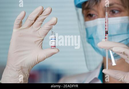 Ärztin mit OP-Maske und in Handschuhen mit Impfampulle und Spritze. Impfung während der COVID-19-Pandemie Stockfoto