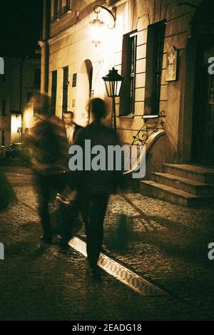 Verschwommene Menschen laufen nachts auf der Straße der antiken Stadt entlang. Monochromes Bild Stockfoto