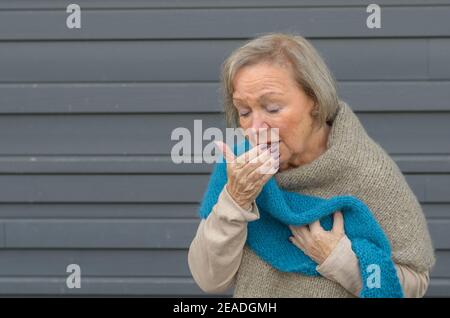 Elegante senior Frau Husten in die Hand und umklammerte ihre Brust in einem Konzept von saisonalen Bronchitis oder Grippe und medizinischen Gesundheitsversorgung, grau mich Stockfoto