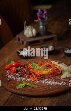 Vertikale Aufnahme einer köstlichen Gourmet-Scheibe Lasagne Bolognese Auf einem Holzbrett Stockfoto
