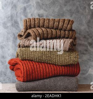 Stapel von gefalteten Strickpullover und Schals aus warmer Wolle auf grauem Hintergrund. Saison der warmen Kleidung. Modekonzept Stockfoto