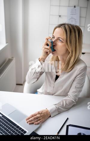 Geschäftsfrau mit Asthma-Inhalator an ihrem Schreibtisch im Büro Stockfoto