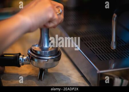 Barista macht Kaffee von Hand aus der Maschine, presst gemahlenen Kaffee mit Tamper. Stockfoto