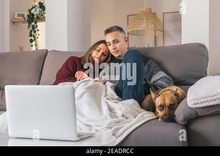 Romantisches junges Paar und ihr Hund zu Hause gemütlich, entspannen auf der Couch, während Sie Filme auf Laptop. Lebenskonzept für Paare Stockfoto