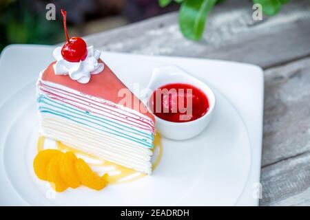 Rainbow Crepe Kuchen und eine Kirsche mit Erdbeersoße auf Holztisch Hintergrund. Stockfoto