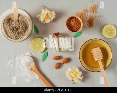 Natürliche Hautpflegeprodukte: Backpulver, Tonpulver, brauner Zucker, Mandelöl. Bunte Hintergrund von Naturkosmetik und Blumen. Natürliche Zutaten Stockfoto