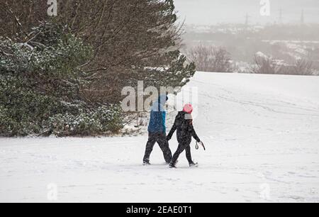 Holyrood Park Edinburgh, Schottland, Großbritannien. 9th. Februar 2021. Der schneebedeckte Holyrood Park ermutigte die Leute, zwischen den Duschen zu spielen und zu trainieren. Pärchen, die in einer schweren Schneedusche spazieren gehen. Stockfoto