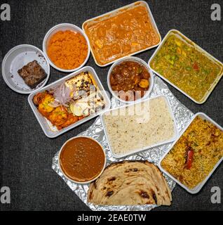 Draufsicht auf eine Vielzahl von indischen Speisen zum Mitnehmen in Plastikbehältern auf einem Stoffhintergrund. Stockfoto
