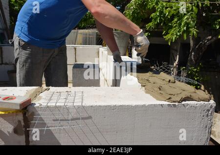 Ein Maurer, Bauunternehmer verlegt eine Ziegelwand aus Beton autoklaviert belüftet Blöcke, Mörtel mit einer Kelle und Verstärkung Drahtgeflecht. Stockfoto