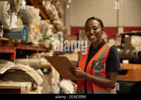 Lächelnde junge afrikanische Lagerarbeiterin, die Inventar macht Stockfoto