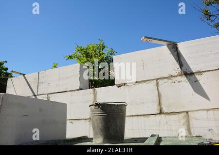 Eine Nahaufnahme von zu Hause hinzufügen, Hauswandkonstruktion aus autoklaviertem Porenbeton Blöcke mit einer Kelle, Mörtel in einem Eimer und Wasserwaage. Stockfoto