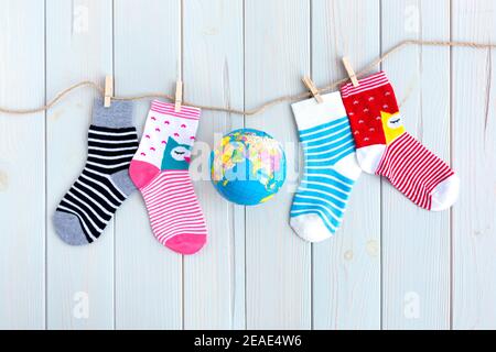 Kindersocken mit Streifen und Farben in Wäscheleine auf Holzhintergrund. In der Mitte befindet sich ein Globus der Welt. World Down Syndrome Day Konzept. Stockfoto