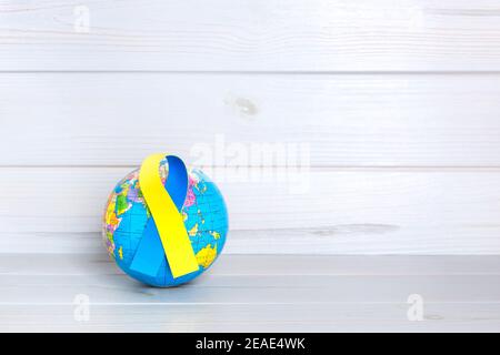 Weltkugel mit gelbem und blauem Band auf Holzhintergrund. World Down Syndrome Day Konzept. Leerzeichen für Text. Stockfoto